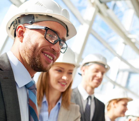 Smiling logistics executives and shipping industry leaders wearing hardhats while standing in a brightly lit atrium.