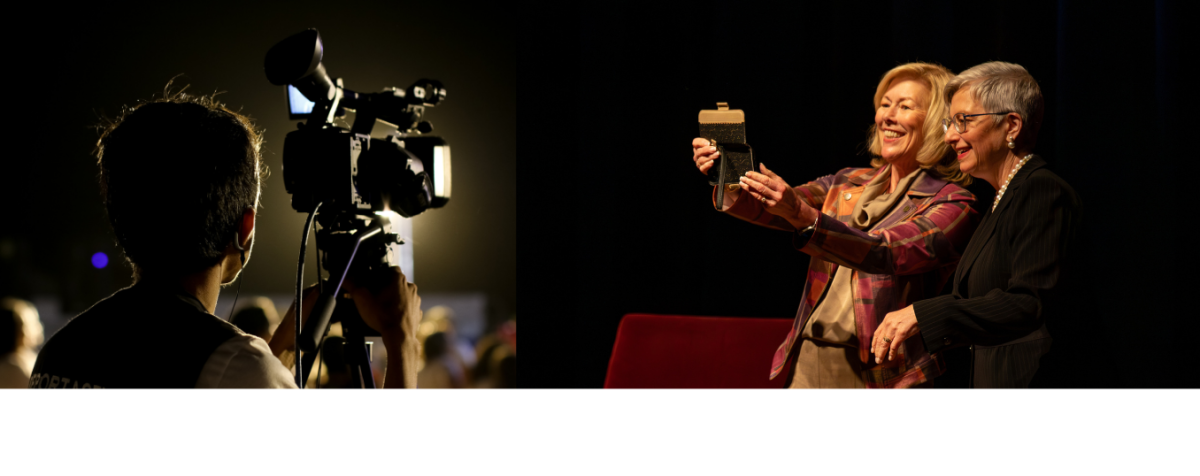 A camera on a tripod in a crowded auditorium on the left; two women taking a selfie on stage on the right